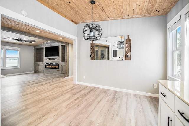 unfurnished dining area featuring light wood finished floors, wooden ceiling, a fireplace, and baseboards