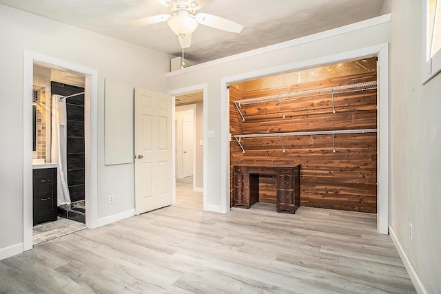 unfurnished living room featuring baseboards, wooden walls, a ceiling fan, and wood finished floors