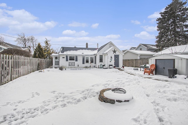 snow covered back of property featuring a fire pit and a storage unit