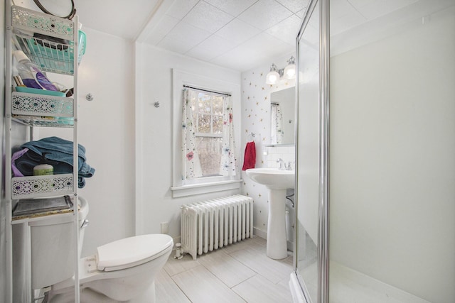 bathroom featuring radiator, a shower with shower door, sink, and toilet