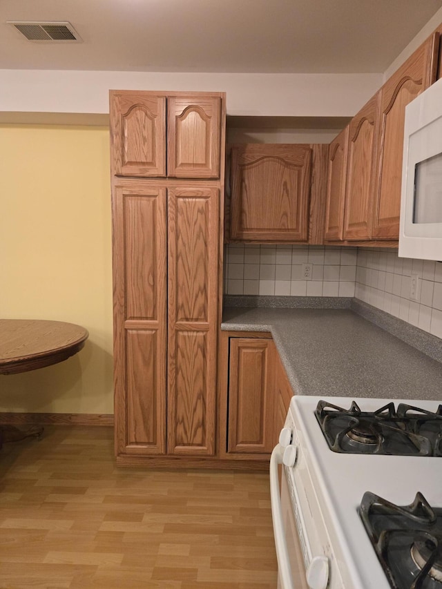 kitchen with decorative backsplash, white appliances, and light hardwood / wood-style flooring