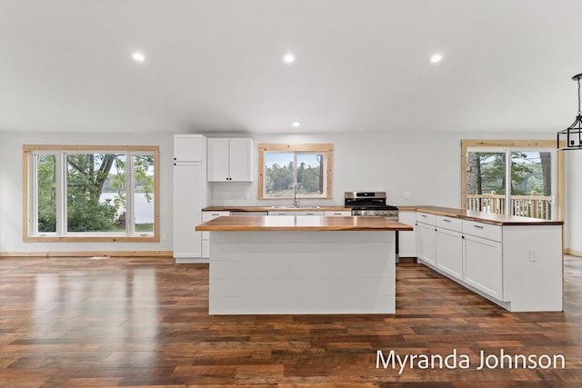 kitchen featuring a kitchen island, sink, hanging light fixtures, stainless steel range oven, and white cabinets