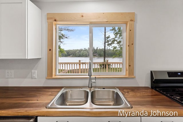 kitchen with stainless steel range oven, white cabinetry, a water view, and sink