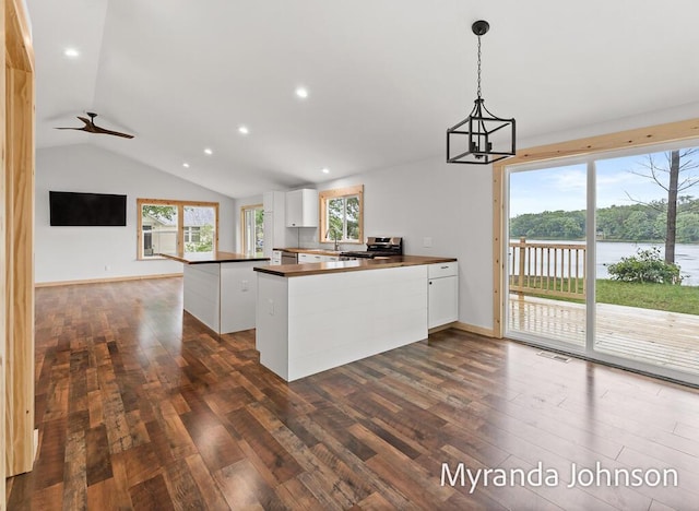 kitchen with kitchen peninsula, hanging light fixtures, stainless steel stove, a water view, and white cabinets