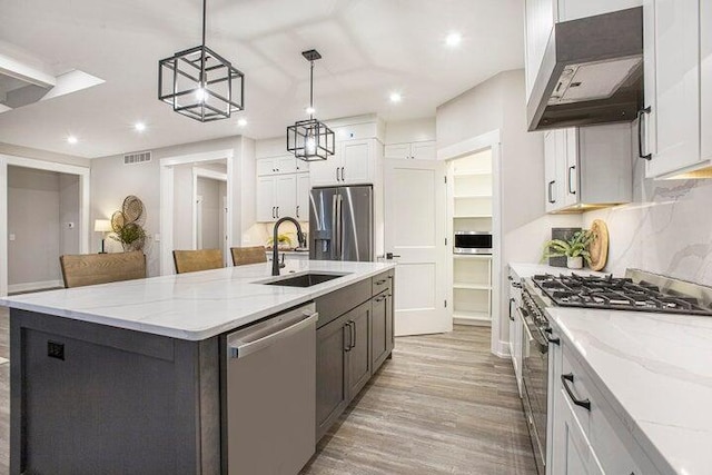 kitchen featuring pendant lighting, stainless steel appliances, an island with sink, custom range hood, and white cabinetry