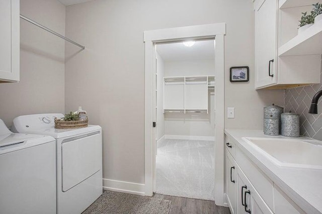 clothes washing area with cabinets, wood-type flooring, washer and clothes dryer, and sink