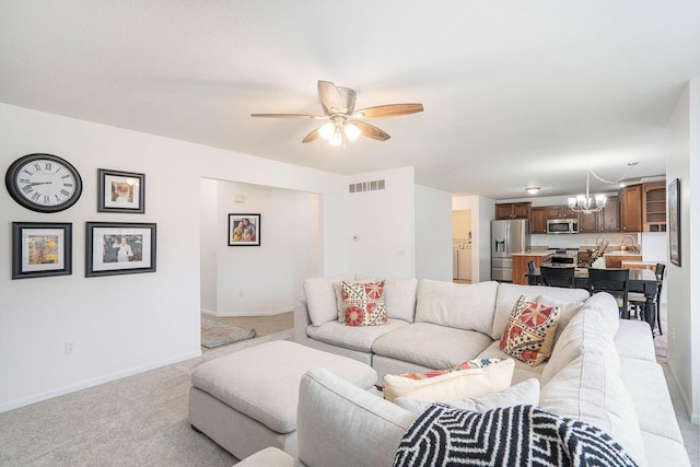 carpeted living room featuring ceiling fan with notable chandelier