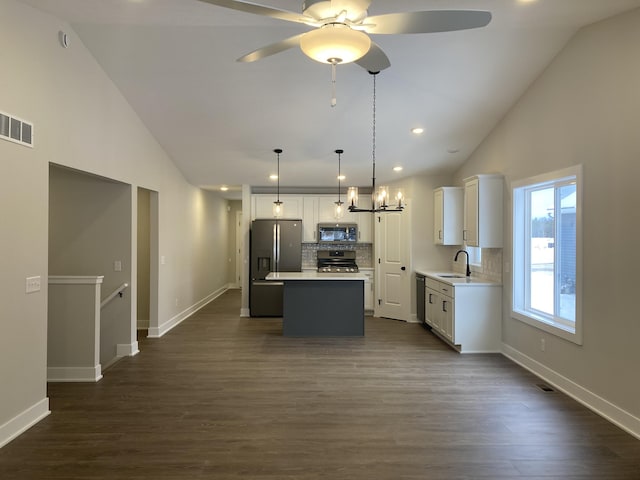 kitchen with appliances with stainless steel finishes, hanging light fixtures, dark wood-type flooring, a kitchen island, and tasteful backsplash