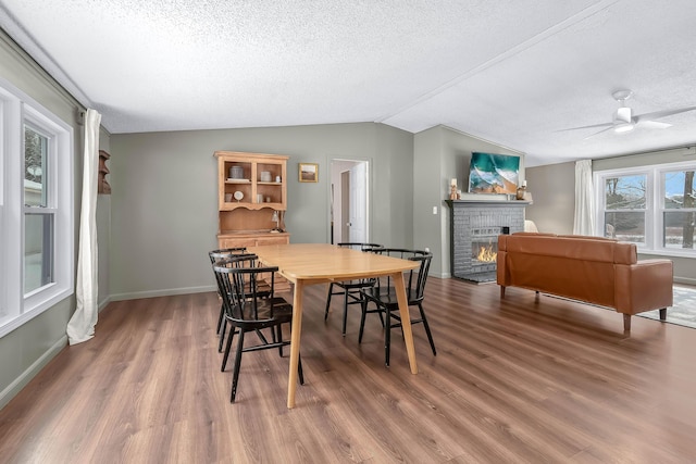 dining room featuring wood-type flooring, vaulted ceiling, a textured ceiling, ceiling fan, and a fireplace