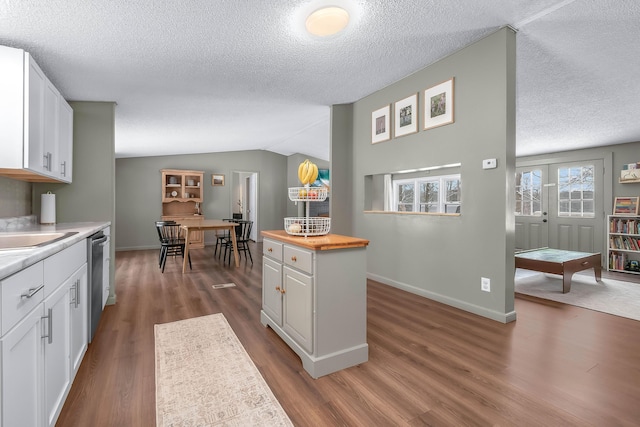 kitchen featuring dark wood-type flooring, vaulted ceiling, dishwasher, and white cabinets