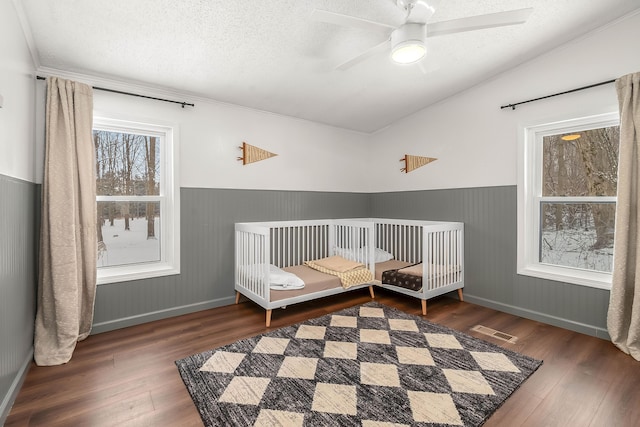 bedroom featuring lofted ceiling, dark hardwood / wood-style flooring, ceiling fan, a crib, and a textured ceiling