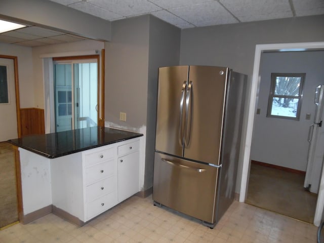 kitchen featuring stainless steel fridge, white cabinetry, and a paneled ceiling