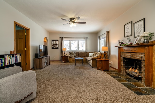 living room featuring a textured ceiling, dark colored carpet, a brick fireplace, and ceiling fan