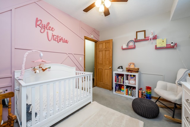 bedroom featuring light carpet, ceiling fan, and a nursery area