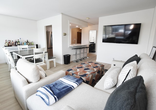 living room featuring light wood-type flooring, ornamental molding, and indoor wet bar