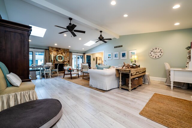 living room featuring lofted ceiling with skylight, a fireplace, ceiling fan, and light hardwood / wood-style flooring