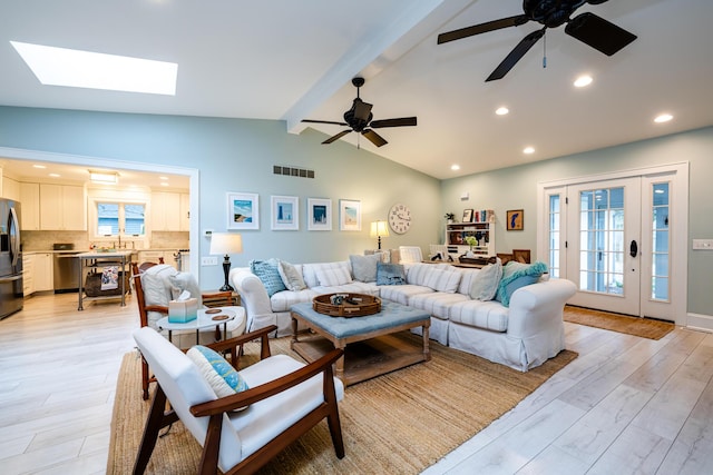 living room with ceiling fan, vaulted ceiling with skylight, and light wood-type flooring