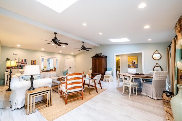 living room with ceiling fan, vaulted ceiling with skylight, and light hardwood / wood-style floors