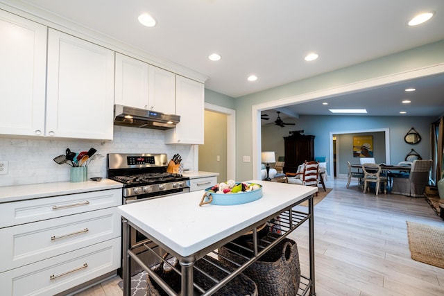 kitchen with stainless steel gas range oven, light hardwood / wood-style flooring, decorative backsplash, and white cabinetry