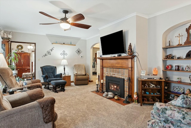 carpeted living room with ceiling fan, crown molding, and a brick fireplace