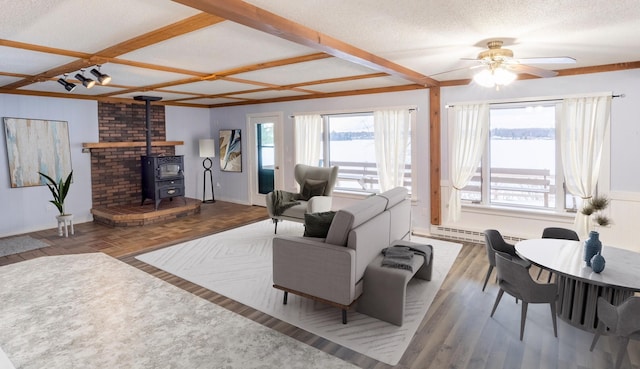 living room featuring a textured ceiling, wood-type flooring, a wood stove, ceiling fan, and coffered ceiling