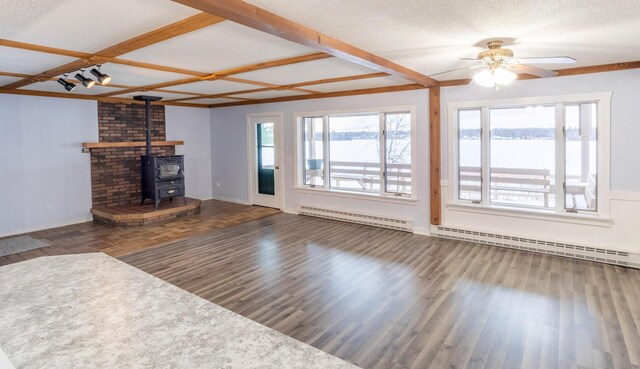 unfurnished living room with dark wood-type flooring, a wood stove, a baseboard heating unit, and ceiling fan