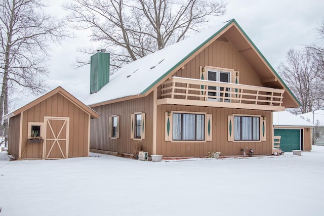 snow covered rear of property featuring a garage and a balcony