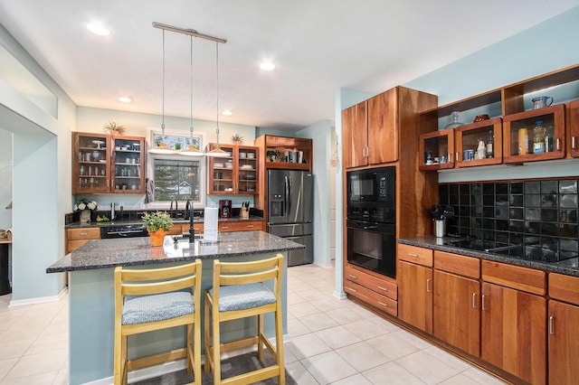 kitchen with tasteful backsplash, black appliances, a kitchen bar, hanging light fixtures, and a kitchen island with sink