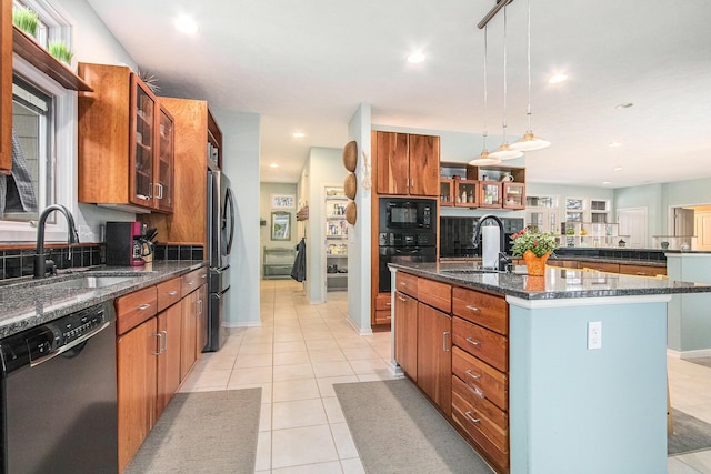 kitchen featuring light tile patterned floors, an island with sink, black appliances, pendant lighting, and sink