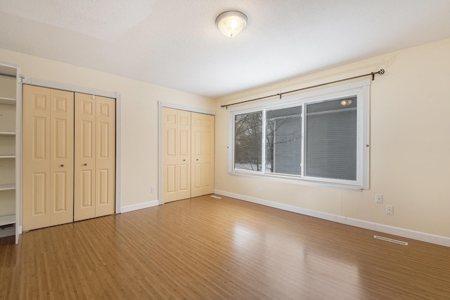 unfurnished bedroom featuring a textured ceiling, two closets, and hardwood / wood-style floors