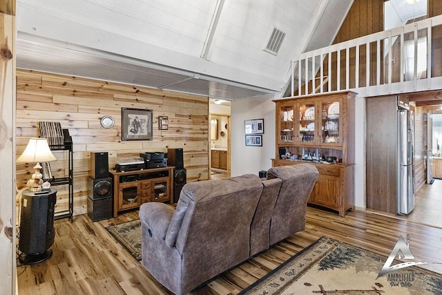 living room with a towering ceiling, wooden walls, and light hardwood / wood-style flooring