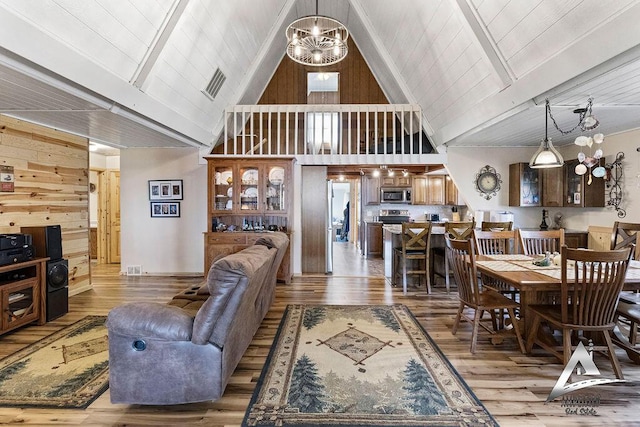 living room featuring wood walls, beamed ceiling, light wood-type flooring, high vaulted ceiling, and a chandelier