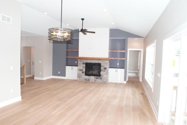 unfurnished living room featuring a stone fireplace, vaulted ceiling, light hardwood / wood-style floors, built in shelves, and ceiling fan with notable chandelier