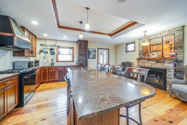 kitchen with black gas range oven, a tray ceiling, and an island with sink