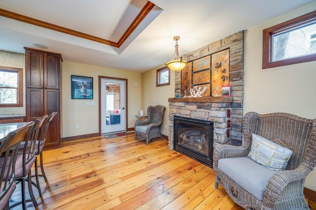 sitting room featuring a tray ceiling, light hardwood / wood-style floors, crown molding, and a stone fireplace