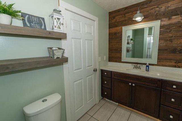 bathroom with toilet, tile patterned floors, wooden walls, and vanity