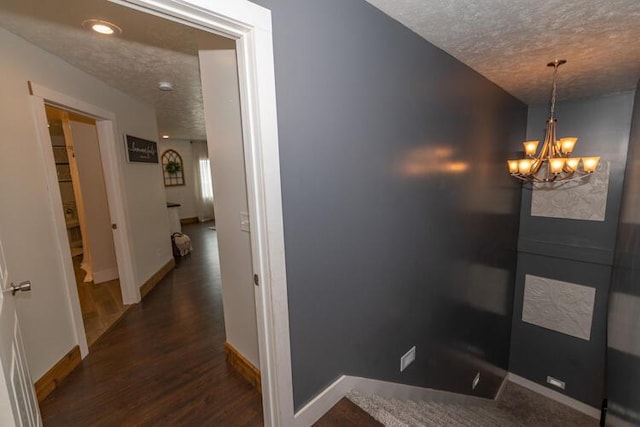 corridor featuring a textured ceiling, dark wood-type flooring, and a chandelier