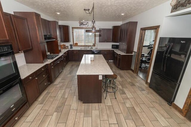 kitchen with a textured ceiling, a kitchen bar, hanging light fixtures, a kitchen island, and black appliances