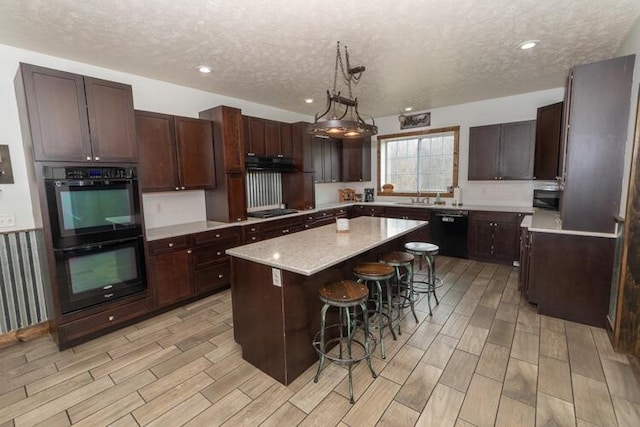 kitchen featuring a kitchen breakfast bar, black appliances, a center island, pendant lighting, and a textured ceiling