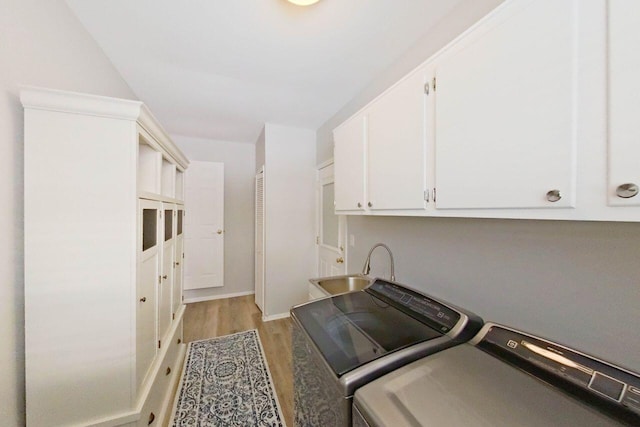 clothes washing area featuring sink, washing machine and dryer, light hardwood / wood-style floors, and cabinets