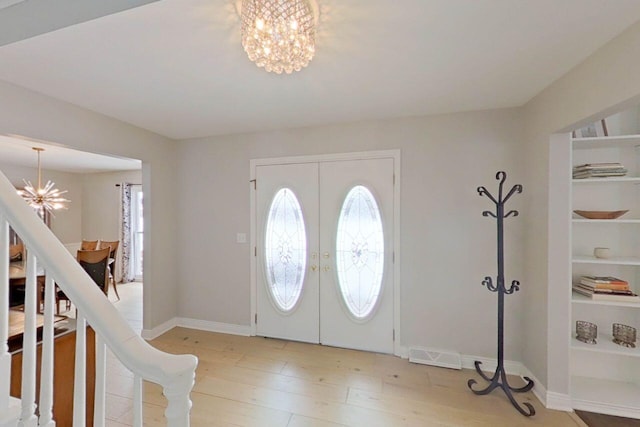 foyer entrance with french doors, an inviting chandelier, and light wood-type flooring