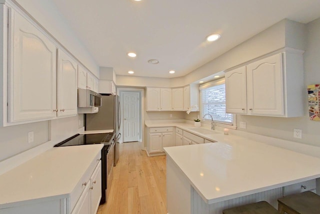 kitchen with electric stove, light hardwood / wood-style floors, kitchen peninsula, sink, and white cabinetry