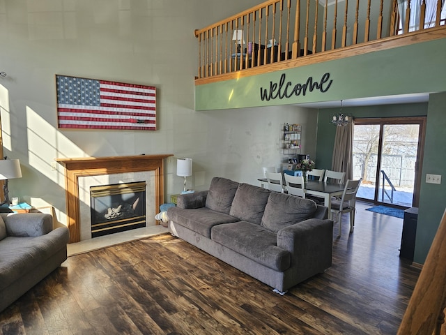 living area featuring dark wood-style flooring, a notable chandelier, a high ceiling, and a premium fireplace