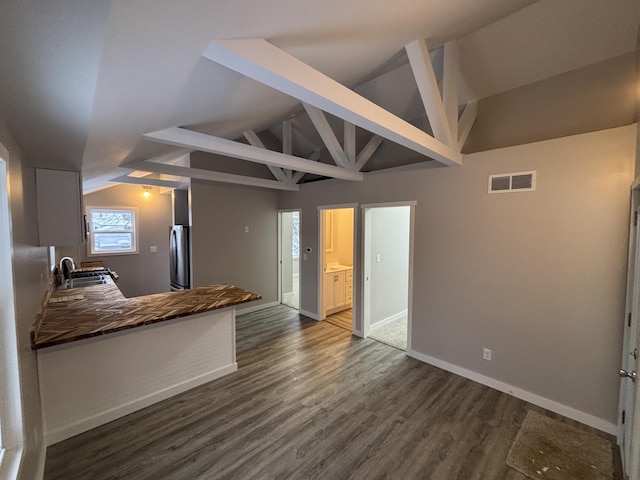 kitchen featuring sink, stainless steel fridge, dark hardwood / wood-style floors, kitchen peninsula, and vaulted ceiling