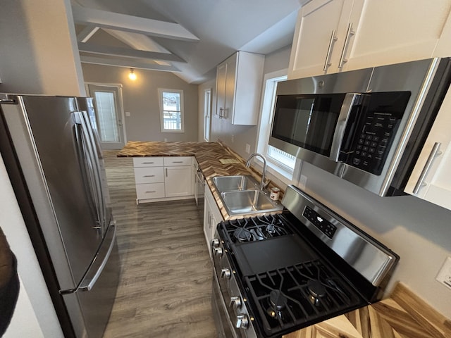 kitchen with hardwood / wood-style flooring, appliances with stainless steel finishes, vaulted ceiling with beams, white cabinets, and sink