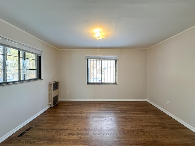 unfurnished room featuring dark hardwood / wood-style floors, heating unit, ornamental molding, and a healthy amount of sunlight