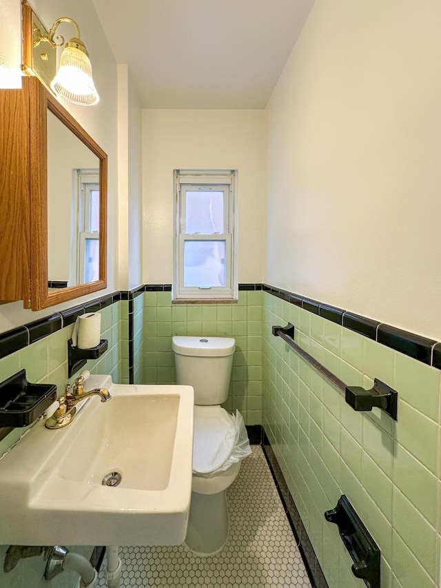 bathroom with toilet, tile patterned flooring, tile walls, and sink