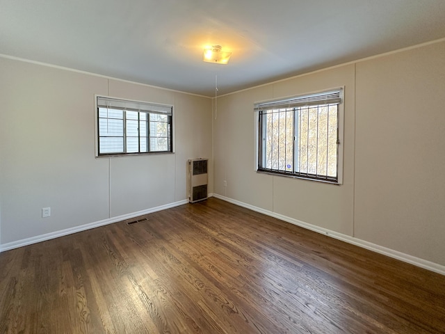 unfurnished room with dark hardwood / wood-style flooring, heating unit, ornamental molding, and plenty of natural light