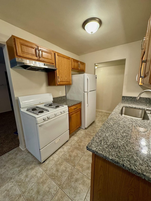 kitchen with white appliances, dark stone counters, sink, and light tile patterned floors