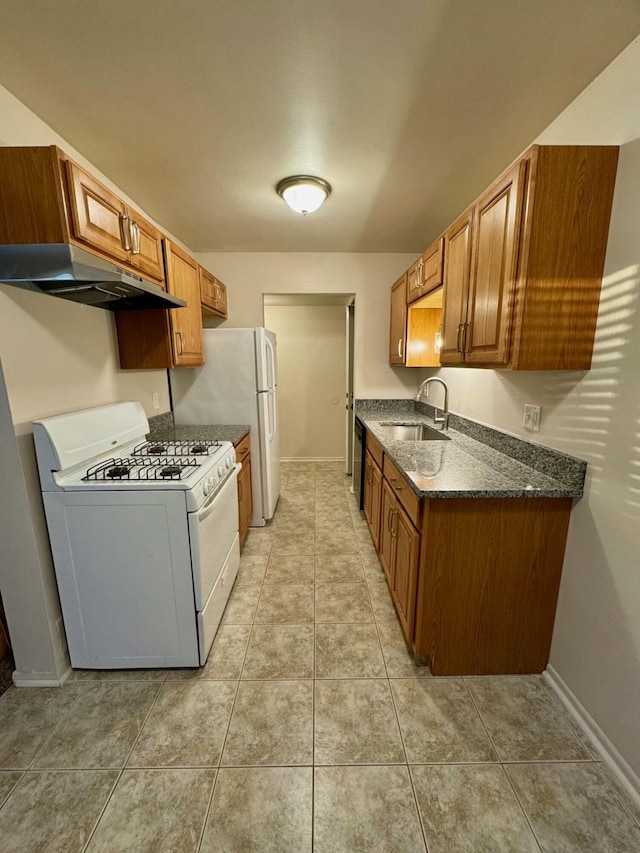 kitchen featuring dark stone counters, white range with gas stovetop, light tile patterned floors, and sink